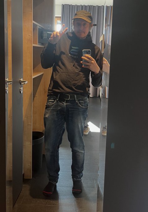 A man wearing a cap and black hoodie takes a mirror selfie, with the "ALPENGLOW" text visible on his clothing. The image ties into his post as a personal introduction while promoting Solana's Alpenglow migration guide and TXV1 upgrade.