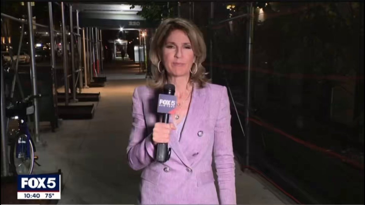 The image features a woman wearing a purple blazer, standing in front of a microphone while holding it up to her mouth. She appears to be talking into the microphone or conducting an interview. The background shows a city street with buildings visible behind her. There is also a bicycle parked nearby. The post that includes this image has the text "me and my unemployed homies doing “nothing” on a Tuesday with a bag full of $neet". This suggests that the woman might be discussing or reporting on an issue related to financial struggles, possibly involving her own family members who are facing similar challenges.