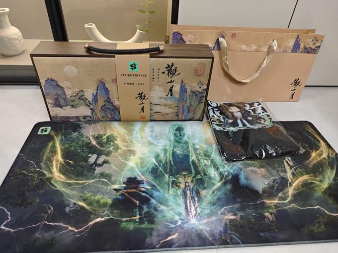 A promotional gift set from 'STRIKE FINANCE' featuring traditional Chinese landscape artwork, including a box, tote bag, and fantasy-themed gaming mat.