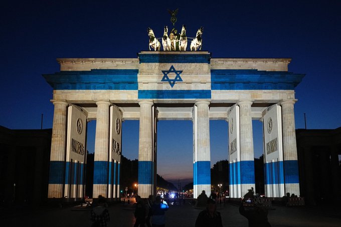 The Brandenburg Gate in Berlin is illuminated in the blue and white colors and design of the Israeli flag at dusk, featuring the Star of David.