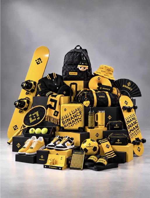 A collection of Binance-branded merchandise in the brand's signature black and yellow color scheme, including a snowboard, backpack, jacket, suitcase, skateboard, sneakers, tennis racket, soccer ball, boxing gloves, and fan, all featuring the Binance logo and "BINANCE" text. The image complements the post by showcasing the diverse range of Binance co-branded merchandise, asking followers to pick their favorite "MVP peripheral" from the lineup.