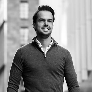 A black-and-white portrait of a smiling bearded man wearing a dark quarter-zip sweater, likely representing Michaël van de Poppe, one of the traders mentioned in the post about bullish Solana price predictions.