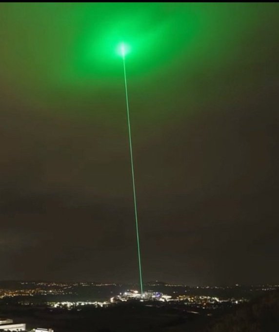 A bright green laser beam projects into the night sky over a city landscape.