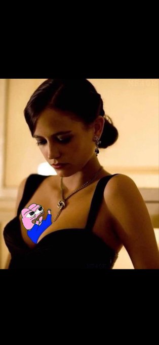 A woman with dark hair in a low bun, wearing a black dress and a silver necklace, looks downward, with a cartoon Patrick Star sticker obscuring part of her chest.