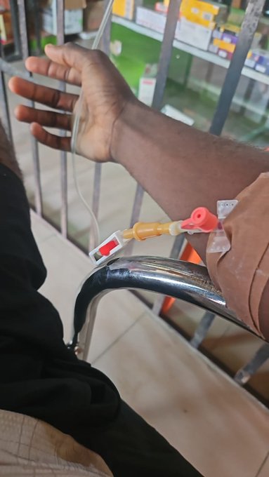 A person's arm is shown with an IV line and medical tubing, appearing to be a patient receiving treatment in a hospital setting.
