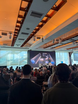 The image shows an audience seated in a modern event space with orange-lit ceiling beams, watching a presentation on stage featuring the "KSA" logo on a large screen, reflecting the Primary VC Summit referenced in the post about the growing buzz around hardware, AI infrastructure, and quantum resilience investments.