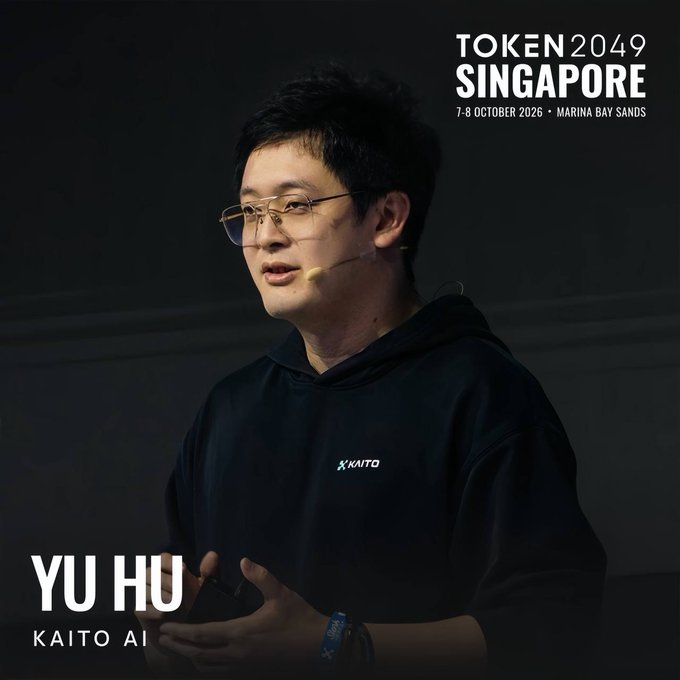 Yu Hu, founder of Kaito AI, is shown speaking at a podium wearing a black Kaito-branded hoodie and headset microphone. The image features promotional text for TOKEN2049 Singapore (October 7-8, 2026, Marina Bay Sands), aligning with his scheduled keynote on October 8 about social media as a global trading floor.