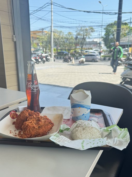 A meal of fried chicken and rice sits on a tray with a bottle of "Tohbar" soda at an outdoor table in Bali. The post highlights enjoying a "Crazy Thursday" meal abroad with friends, paid seamlessly using the Gate Card.