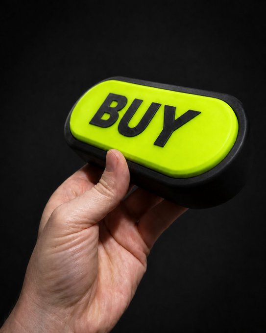 A hand holds a bright yellow-green button with the word "BUY" printed in bold black letters against a dark background.