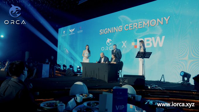 A formal 'SIGNING CEREMONY' event between ORCA and JBW with a large screen backdrop, showing executives at a signing table with a VIP dining area in the foreground and 'www.iorca.xyz' displayed.