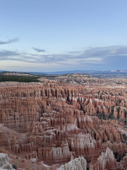 A scenic view of Bryce Canyon's distinctive orange and white hoodoo rock formations stretching across the landscape under a partly cloudy sky.
