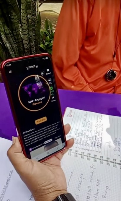 A person holds a smartphone displaying 'OnChainTide' app showing 'S5Ls: Engaged Pioneers' and '1.00009 lt', with handwritten notes visible on the table below.