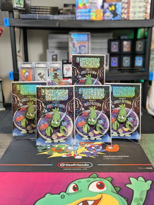 A display of VeeFriends 'Shell's Kitchen' trading cards, appearing to be a limited edition collaboration, arranged on a desk with graded cards visible in the background.