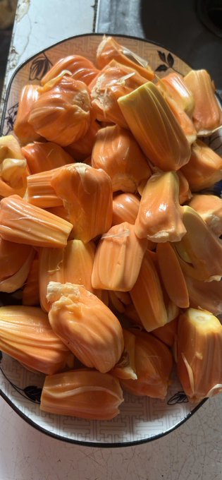 A bowl filled with pieces of bright orange jackfruit, showing the fleshy, ridged texture of the fruit's bulbs.