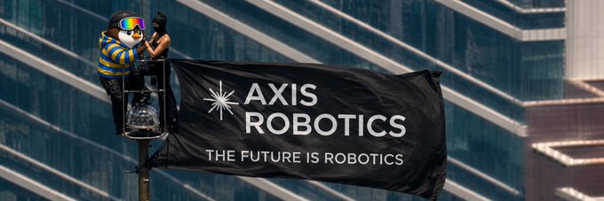 A person in a yellow safety vest and VR headset sits atop a streetlight holding an 'AXIS ROBOTICS' banner that reads 'THE FUTURE IS ROBOTICS'.