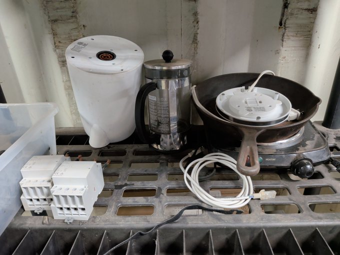 Various discarded or stored household items including a white kettle, French press, cast iron skillet, power strip, cables, and circuit breakers sitting on a plastic pallet.