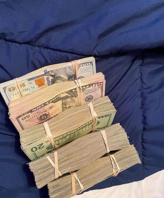 Several thick stacks of U.S. currency, including visible $50 and $20 bills secured with rubber bands, rest on a dark blue comforter—visually reinforcing the caption's urgent message about needing money rather than simply wanting it.