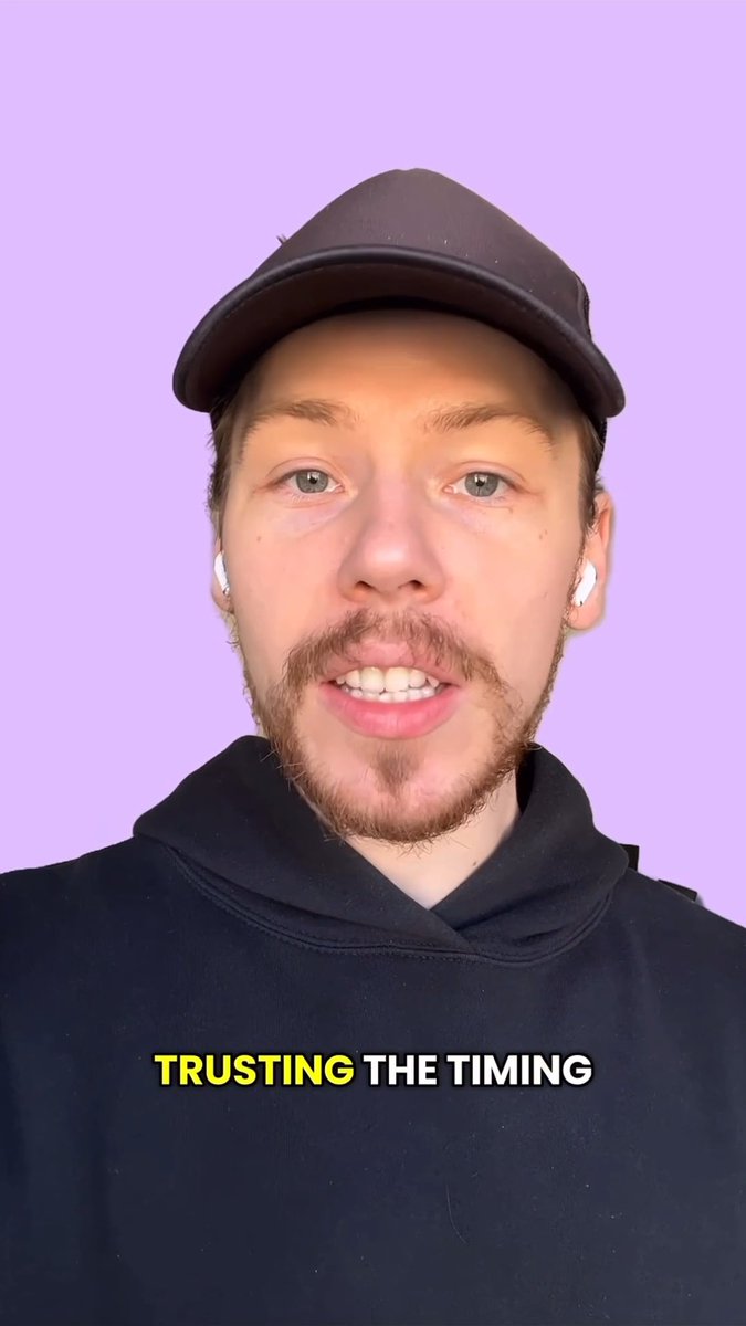 A man wearing a black cap, hoodie, and white earbuds speaks to the camera with the text 'TRUSTING THE TIMING' displayed at the bottom.