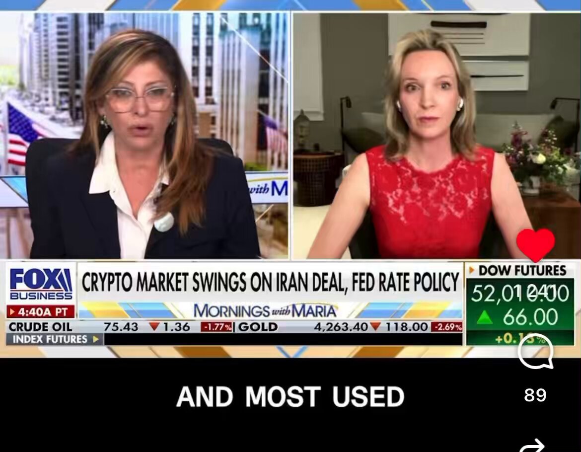 The image shows two women sitting at a table, with one woman wearing glasses and the other wearing a red dress. They are both talking about the crypto market swings on Iran's deal for fed rate policy. The news anchor is reporting that most of the trading activity in the crypto market has been driven by this news.