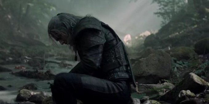A scene of Geralt of Rylima, the white-haired protagonist from The Witcher, kneeling on rocky ground in a misty forest environment.