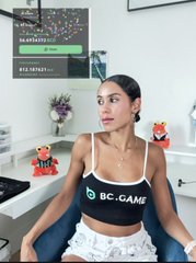 A young woman sitting in a chair wearing a black BC.GAME sports bra in an indoor room with small red decorative figures.