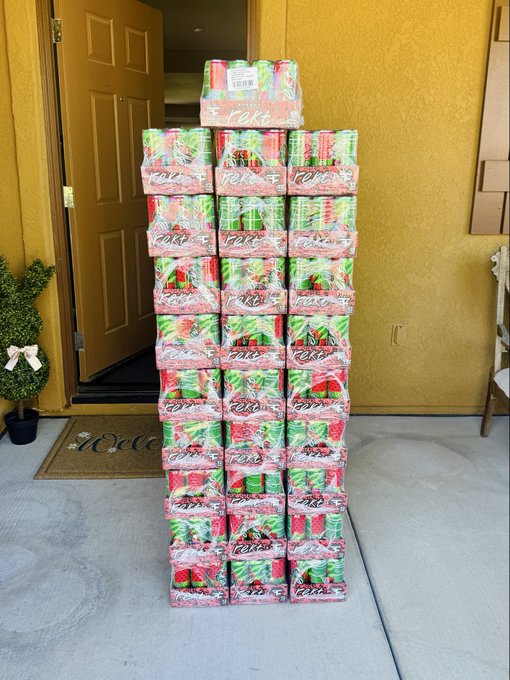 A tall pyramid-like stack of Cases brand strawberry soda cans arranged on a porch in front of a doorway with yellow walls.
