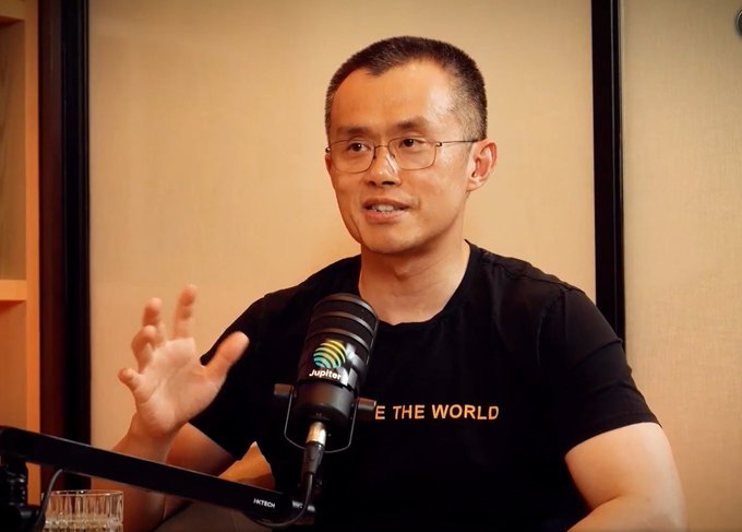 A man with glasses wearing a black 'CHANGE THE WORLD' t-shirt sits at a desk speaking into a microphone labeled 'ASR' in what appears to be a podcast setup.