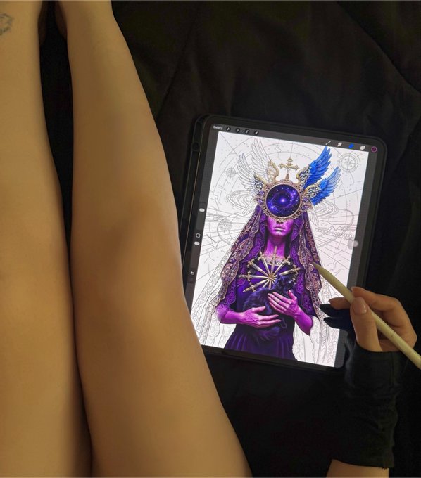 An overhead view of a person holding a stylus, digitally painting a purple-toned mystical figure with a crystal orb for a face on a tablet resting on their lap.