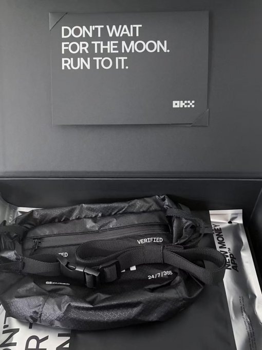 A black OKX-branded bag inside a black box with a card reading 'DON'T WAIT FOR THE MOON. RUN TO IT.' and the OKX logo.