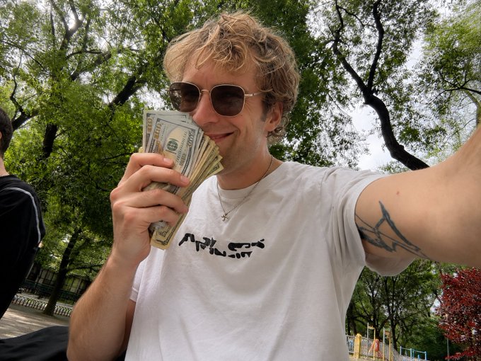 A young man with sunglasses holds a fanned stack of $100 bills near his face while smiling outdoors, his white t-shirt displaying the text "ARMY WILL Y," with a tattoo visible on his outstretched arm and lush green trees behind him.

The image humorously contrasts the post's message about a failed Ethereum "financial experiment" with a playful visual of someone gleefully displaying cash—seemingly celebrating profits or mocking the crypto downturn with traditional money.