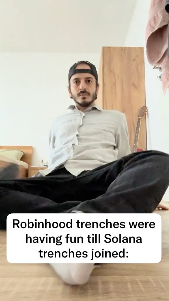 A man sitting on the floor in a room with a guitar in the background, overlaid with text reading 'Robinhood trenches were having fun till Solana trenches joined:'.