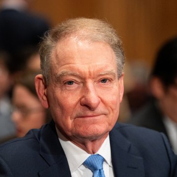 An older man in a dark suit and blue tie, with thinning gray hair, sits in what appears to be a formal hearing or governmental setting. The image likely relates to the SEC's recent decision regarding tokenized stock trading, possibly depicting an SEC official or commissioner involved in shaping the new regulatory framework for on-chain trading of tokenized equities.
