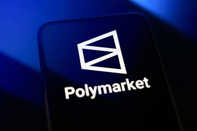 A close-up of a smartphone screen displaying the Polymarket logo, featuring a white geometric diamond design and the word "Polymarket" against a dark blue background.