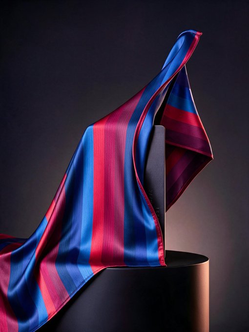 A dramatic, flowing fabric in bold blue and red stripes drapes elegantly over a dark sculptural form, evoking a sense of mystery and anticipation. The striking visual captures the allure of a surprise reveal, perfectly complementing the teasing message of something special on the horizon for 500 million fans.