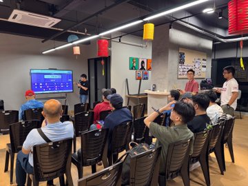 An indoor gathering with people seated in chairs facing a screen, decorated with red Chinese lanterns hanging from the ceiling.