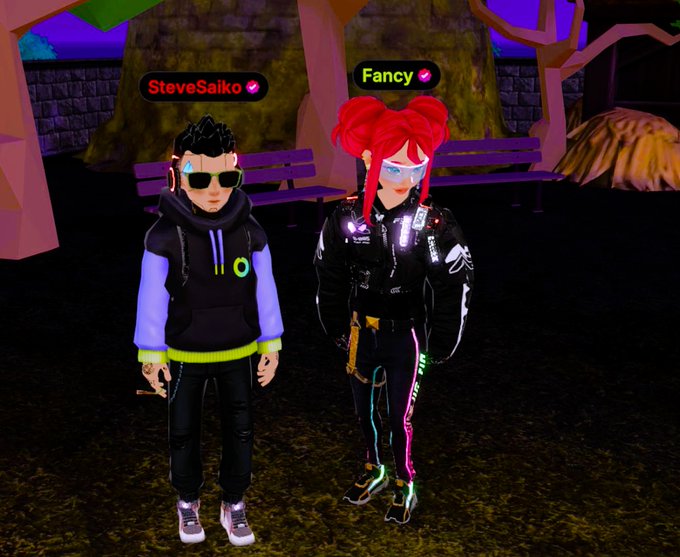 The image features two cartoon characters standing next to each other, both wearing black jackets with neon green stripes. One character has a name tag that reads "Fancy", while the other has a name tag that says "#Decentraland". The background of the image is dark and filled with trees, giving it an immersive feel as if the characters are in a forest or jungle setting.