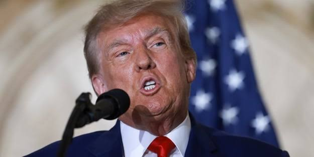 Donald Trump, in front of the US flag, speaks into a microphone, aligning with the post's comparison of his presidency's impact on crypto versus traditional assets.