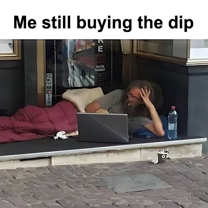 A meme with the text "Me still buying the dip" showing a disheveled person lying on the ground with a laptop, smoking a cigarette, appearing to be in a rough situation.