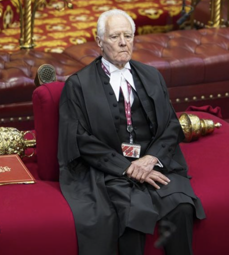 An elderly man, appearing to be a senior figure, sits solemnly in a red ceremonial chair wearing formal black robes with white wing collar attire and a lanyard, likely at a UK parliamentary or state event. The image relates to the post about UK MPs rejecting the "assisted dying" legislation by 16 votes (286 against, 270 in favor), a bill that would have allowed terminally ill adults in England and Wales with fewer than six months to live to seek an assisted death.