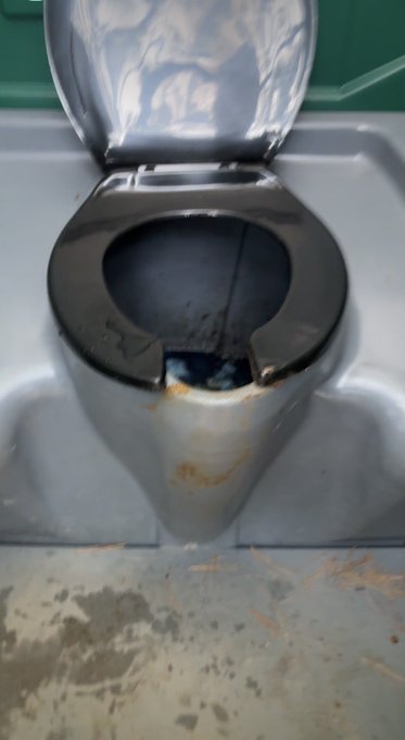 A stainless steel portable toilet with an open lid, showing visible rust stains and a worn floor beneath it.