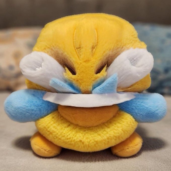 A yellow and blue Psyduck Pokémon plush toy is shown being hugged or pressed down by a pair of hands, looking distressed. The image humorously represents the post's mention of a massive crypto "airdrop" to 99 Nigerians, with the overwhelmed plush symbolizing the absurdity of a 67% "lmao" token bundle being distributed.