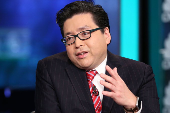 An Asian man wearing glasses, a dark pinstripe suit, and a red striped tie, speaking and gesturing with his hand in what appears to be a television studio.