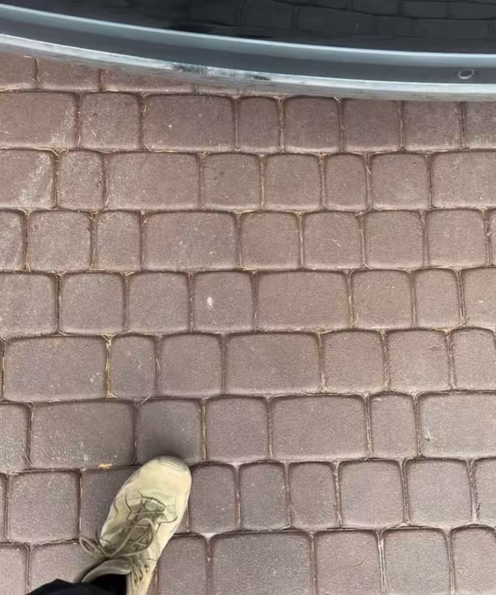 The image features a person's foot stepping onto a brick walkway, which has a unique pattern of small square bricks arranged in rows. The person appears to be wearing brown boots while walking across this interesting surface. In the background, there are two other people partially visible on the right side of the photo. The image also contains text that reads "They say Big Money Never Comes Clean" and "My plan: We'll make millions Then phase II: We'll go full on G mode & will make our first Billion". This suggests a connection between the person's actions in the image, which is walking across the brick walkway, and the post's message about making money.