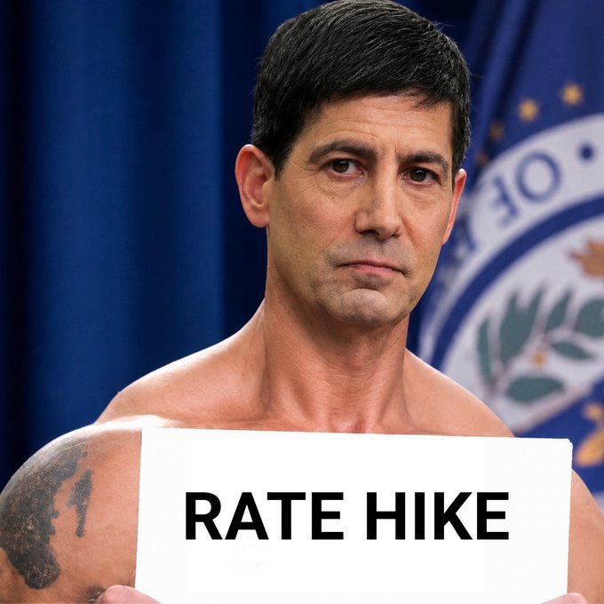 The image shows a shirtless man holding a "RATE HIKE" sign in front of what appears to be an official seal, presented in a mugshot-style format—a humorous and irreverent visual pun playing on the word "hike" (literally showing someone hiking a shirt) to mock the Federal Reserve's 25 basis point interest rate increase.
