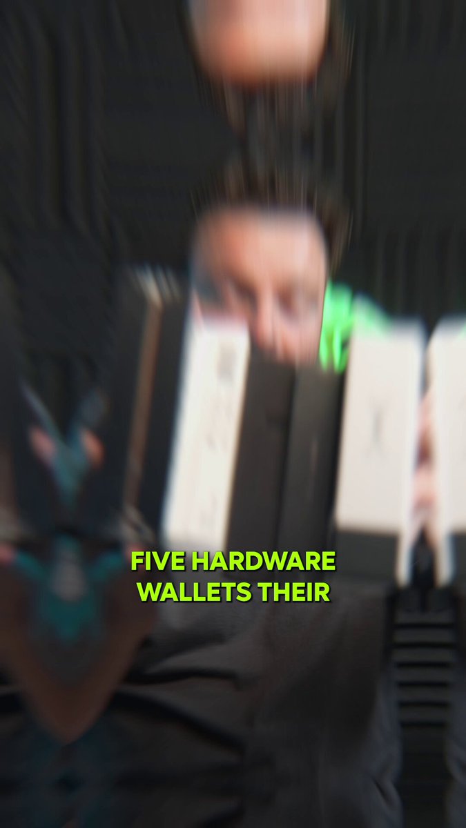 The image features a person holding two hard drives, with the text "Five hardware wallets their" written above them. The person appears to be wearing black clothing and has a green light shining on their face.