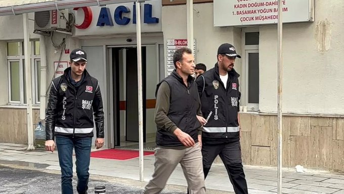 Three police officers in dark vests labeled 'POLIS' escorting a man in a brown jacket out of a building with signage reading 'ACİL' (Emergency), 'KADIN DOĞUM-DAHİLİYE', '1. BASAMAK YOĞUN BAKIM', and 'ÇOCUK MÜŞAHEDE' in Turkish.