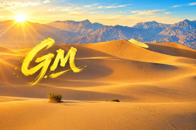 A stunning desert landscape with golden sand dunes at sunset, featuring the letters 'GM' written in gold brushstroke style in the sky.