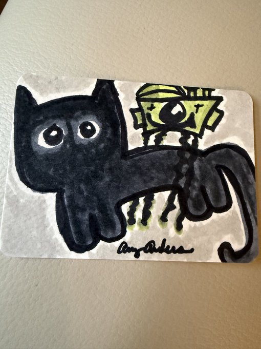 A small artwork on paper depicting a black cat with large eyes and a green mechanical figure, signed 'Amy Akira'.