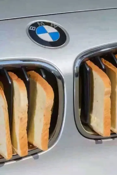A humorous photo of a BMW car grille modified to function as a toaster, with slices of bread popping out of the kidney-shaped vents beneath the iconic blue and white BMW logo.