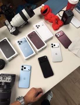A collection of various iPhones in different colors (blue, white, black, pink, and silver) laid out on a table alongside camera equipment, with the post announcing a giveaway where participants pick a number between 20 and 72 for a chance to win a share of $5,000 in prizes.